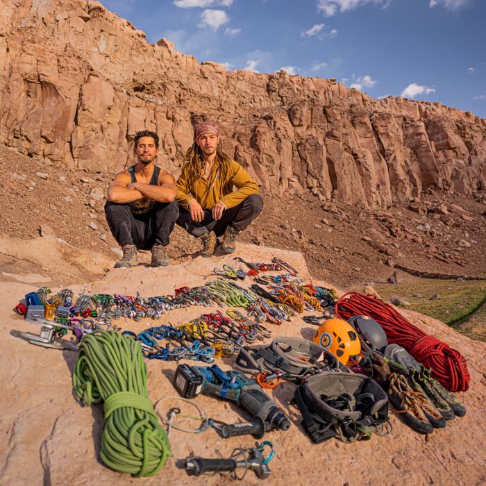 Two climbers crouching behind some trad climbing equipment in Alto El Loa, Northern Chile