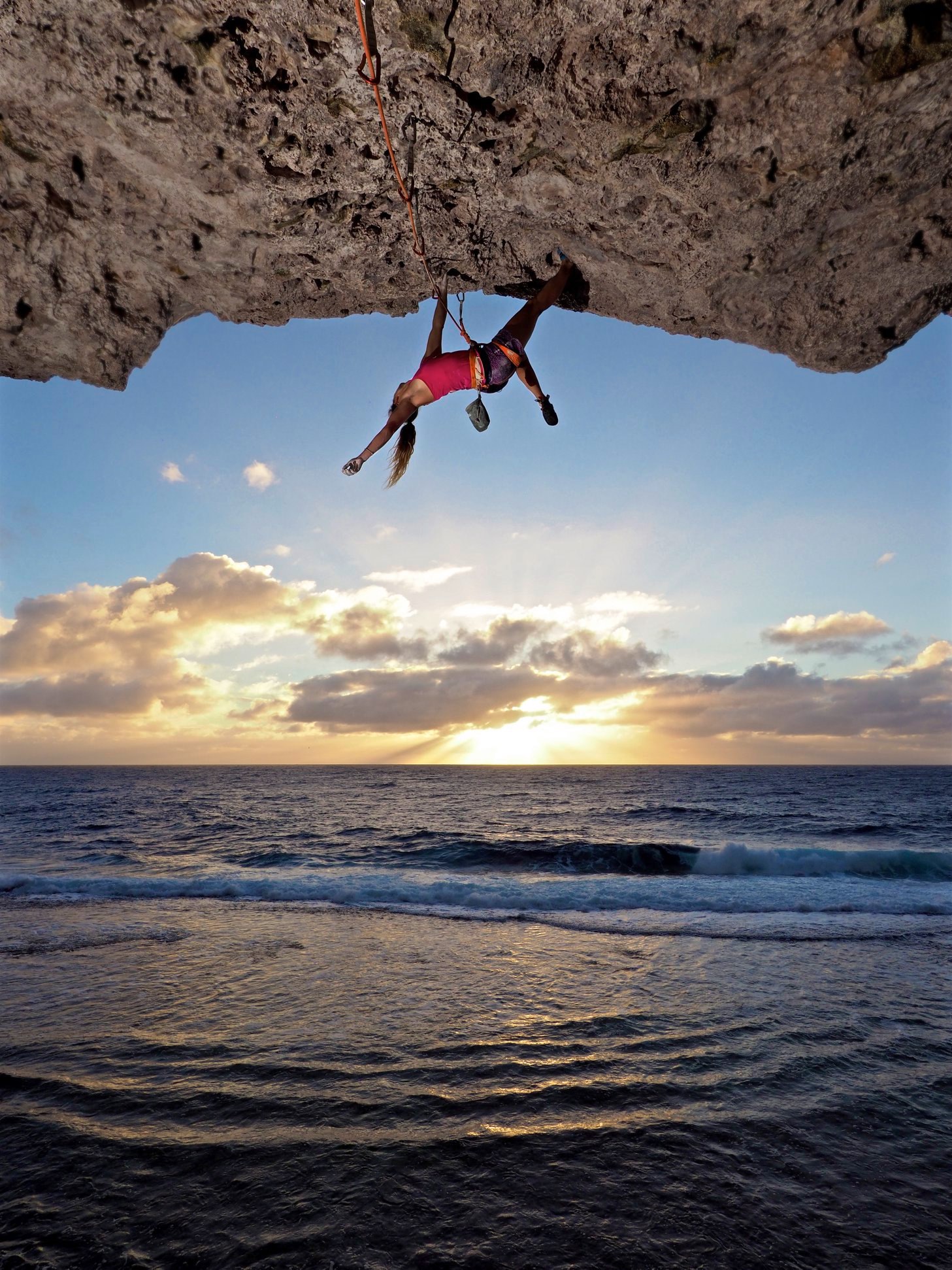 A sport climber rock climbing on the beach at sunset
