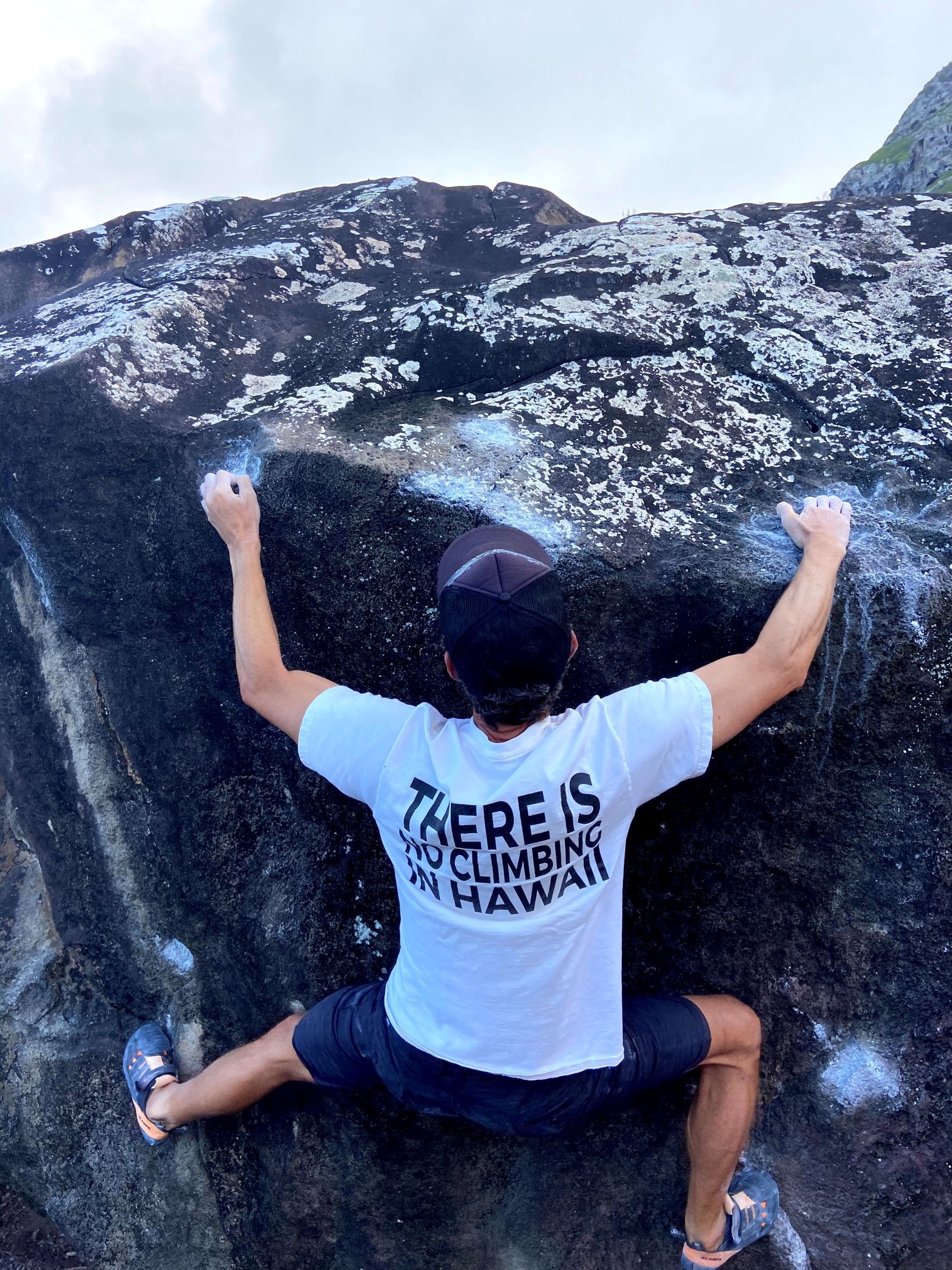 Close up of a person bouldering with a 'There is no Climbing in Hawaii' shirt