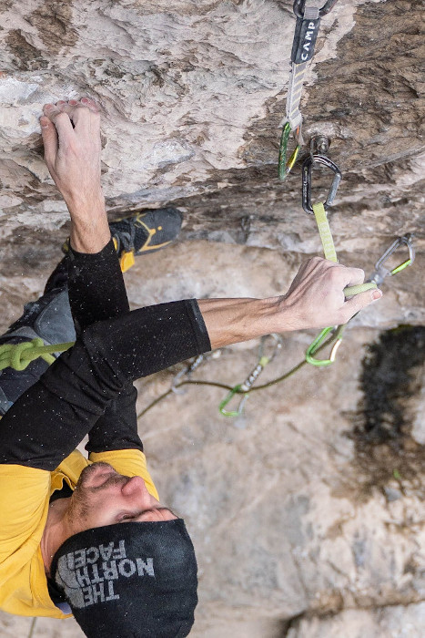 Stefano Ghisolfi clipping a quickdraw while rock climbing in Ceuse