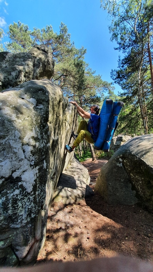 A person climbing in Rocher Canon with a crashpad on their back