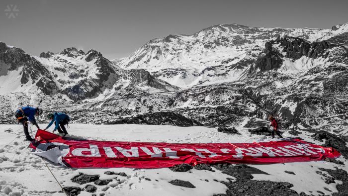 A banner saying 'Salvemos el Maipo' being rolled out on a snowy peak