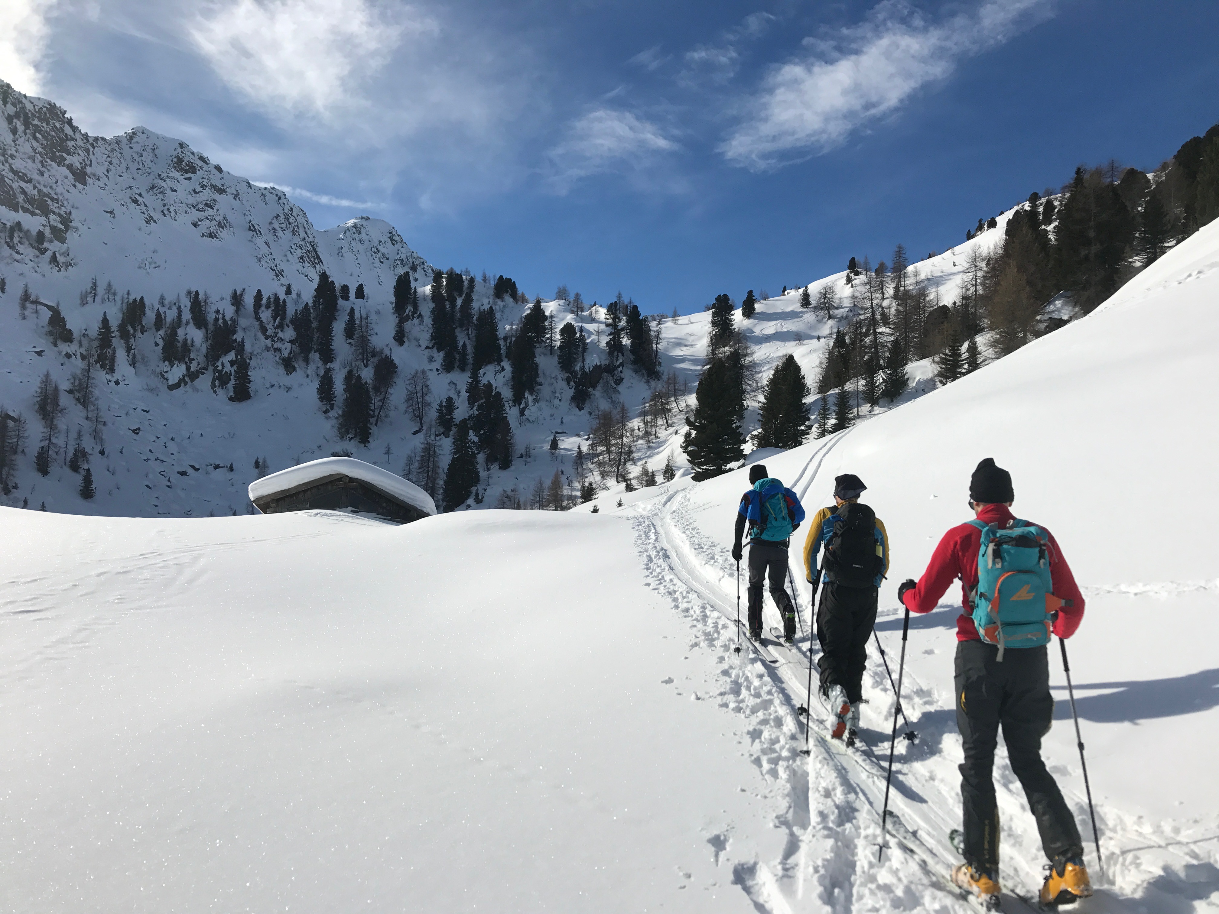 Three ski tourers in a valley in the Dolomities, with a peak in the background