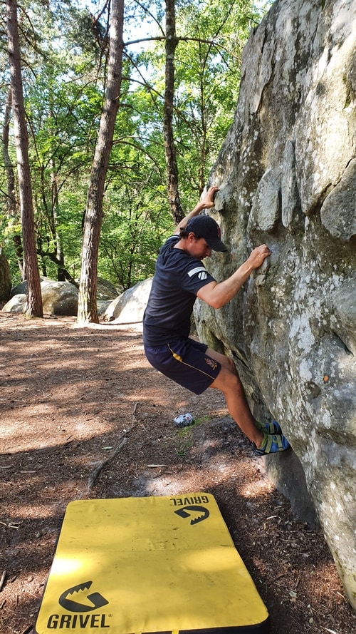 A boulderer on a lowball in Mont Aigu, Fontainebleau