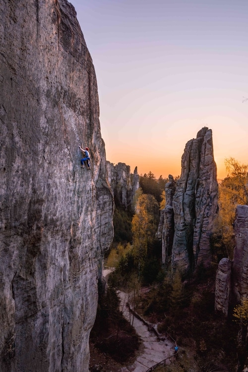 A rock climber on one of the sandstone towers in Cesky Raj, with the sunset in the background