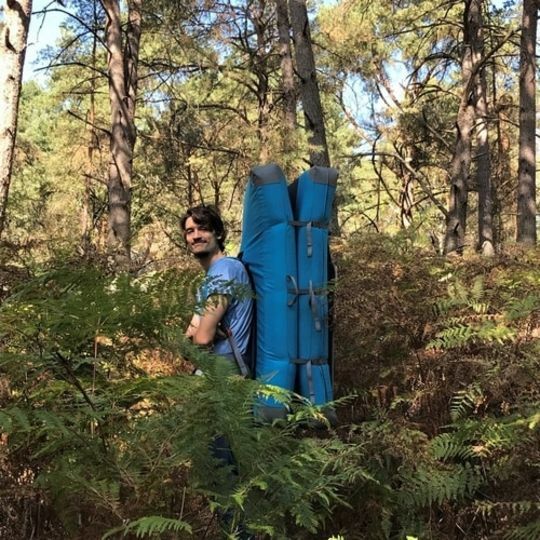 A person standing in the Fontainebleau forest with a crashpad