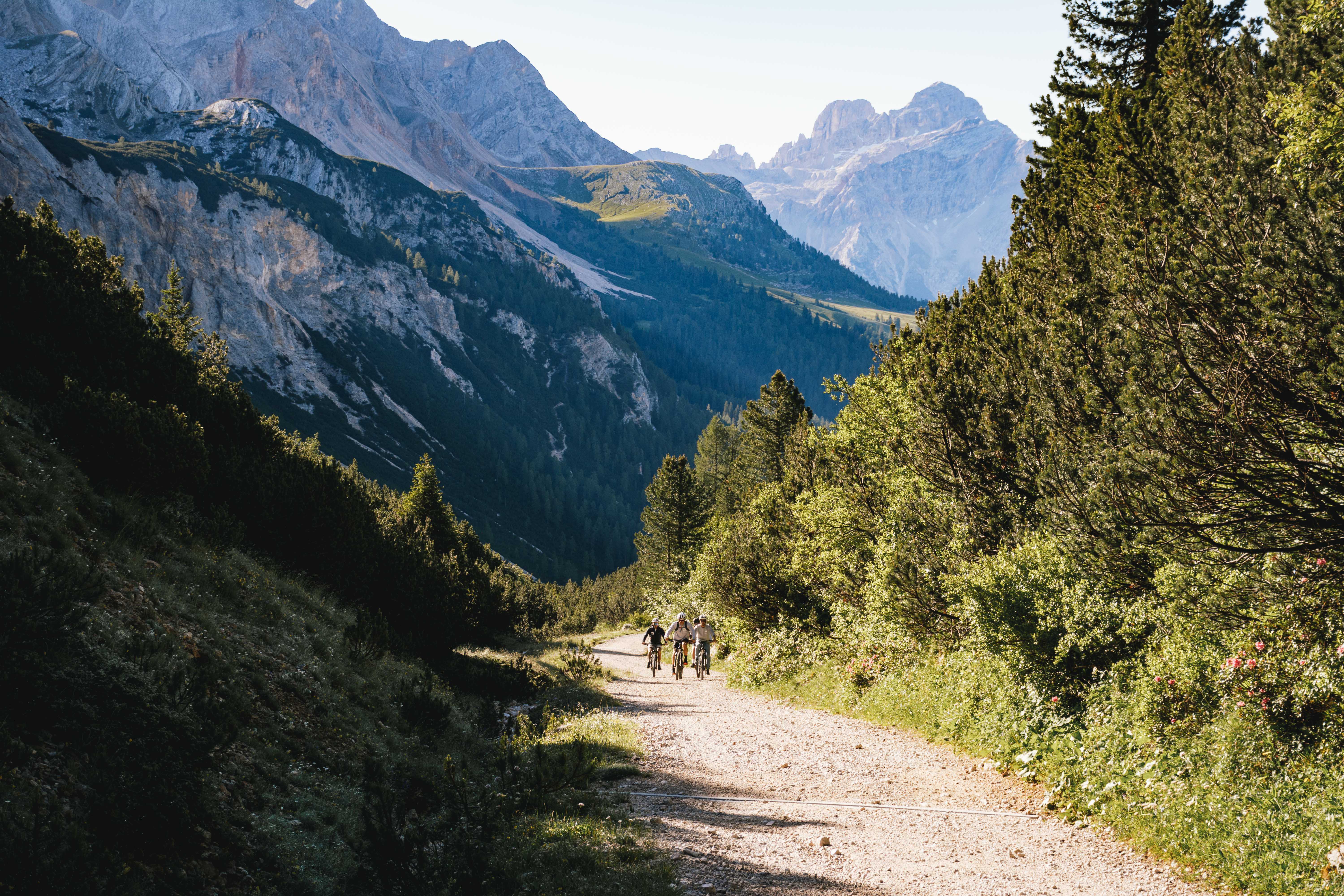 Three people ascending an uphill dirt path on mountain bikes in the Dolomites