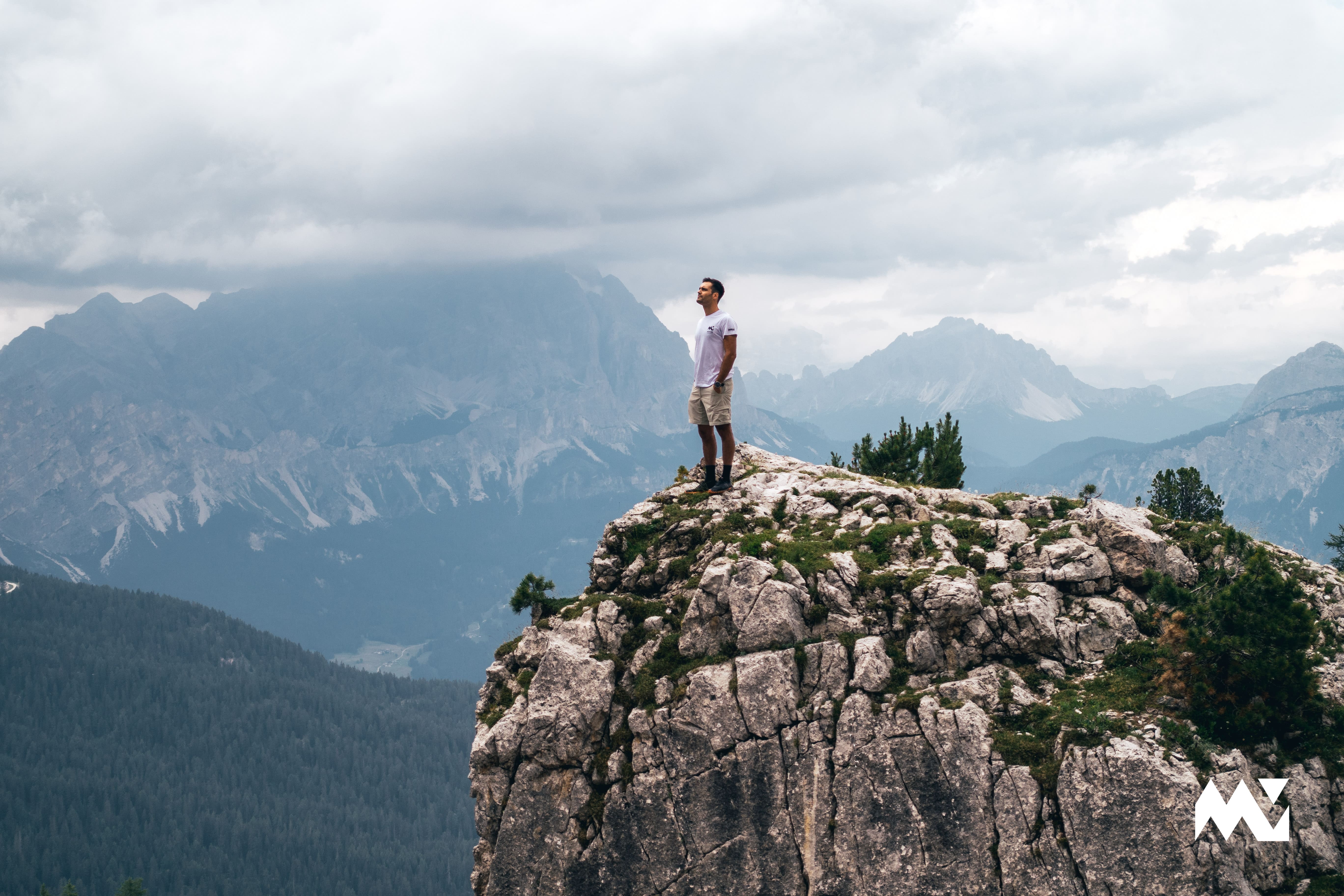 A hiker standing at the top of a mountain with the Dolomites' peaks in the background
