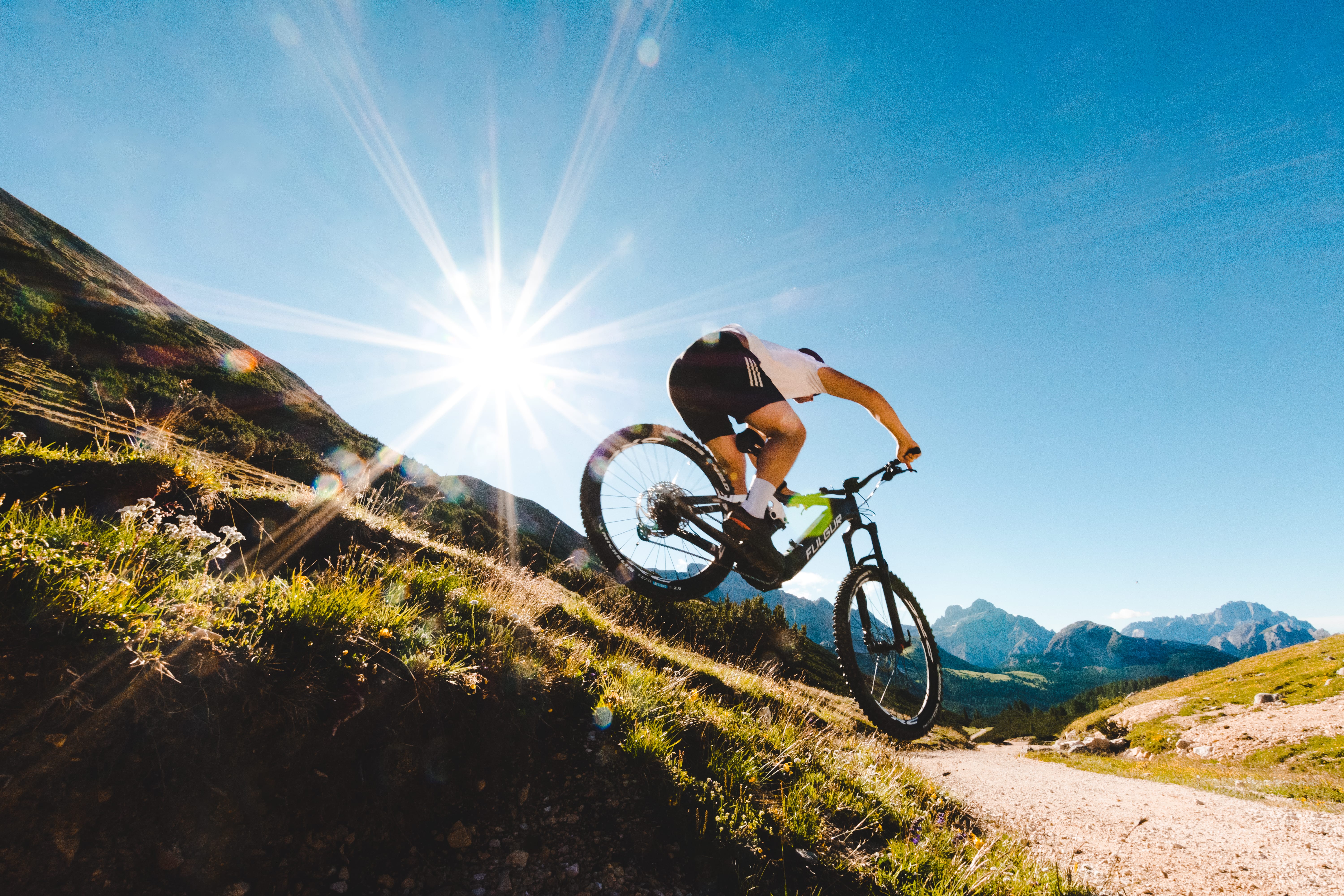 Una persona che fa downhill in mountain bike nelle Dolomiti, con le montagne alle spalle