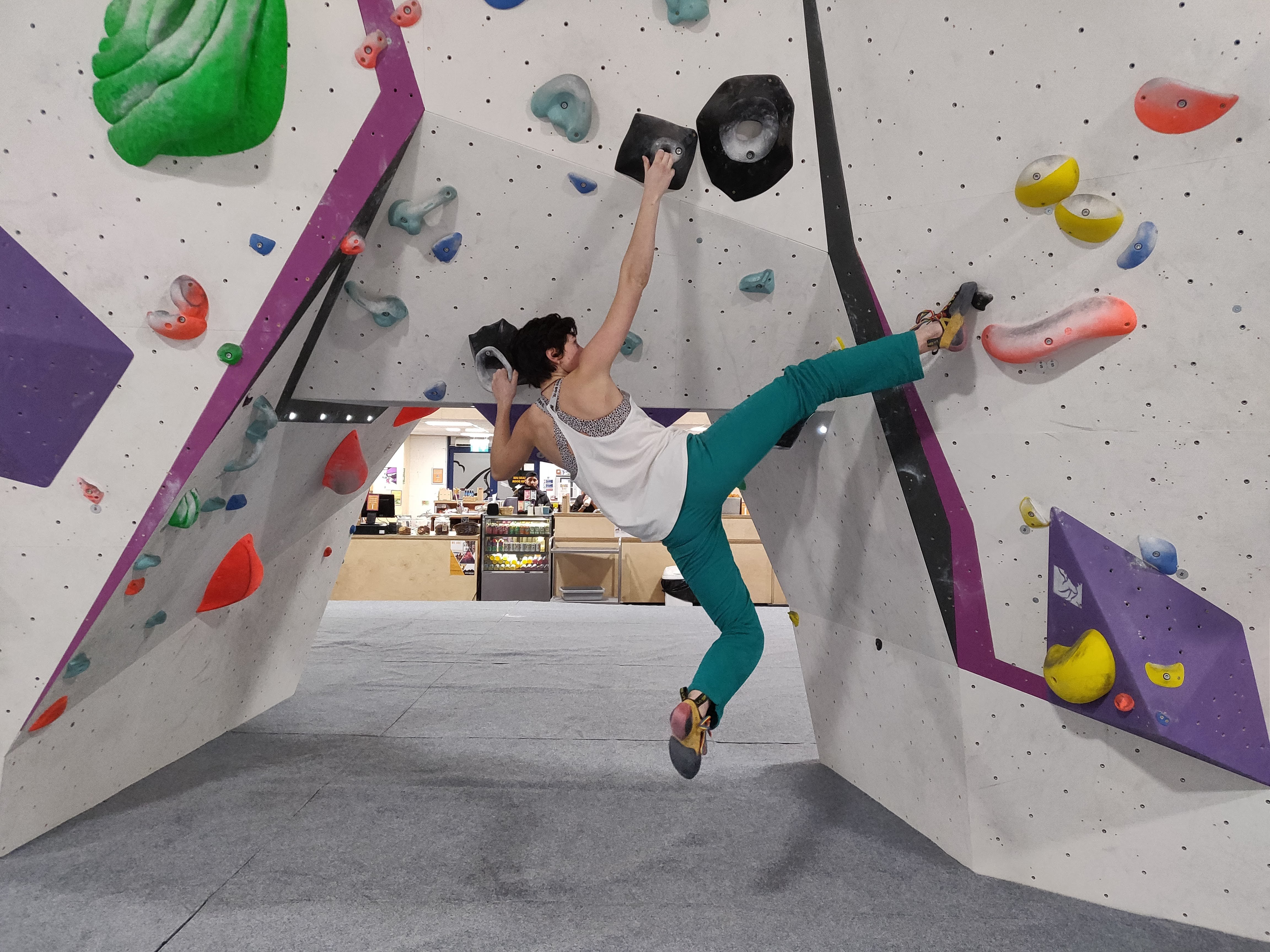 A boulderer in a climbing gym wearing rock climbing trousers and a vest